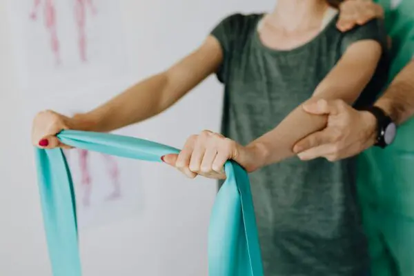 vrouw oefent onder begeleiding met een strekband/elastiek